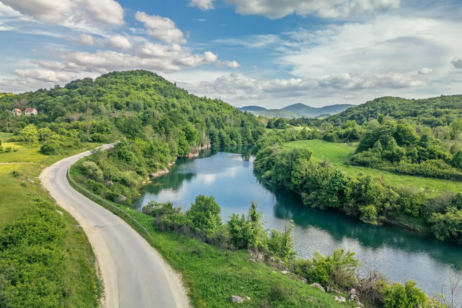 Prazna cesta prati zavoj zelene rijeke, snimljeno dronom