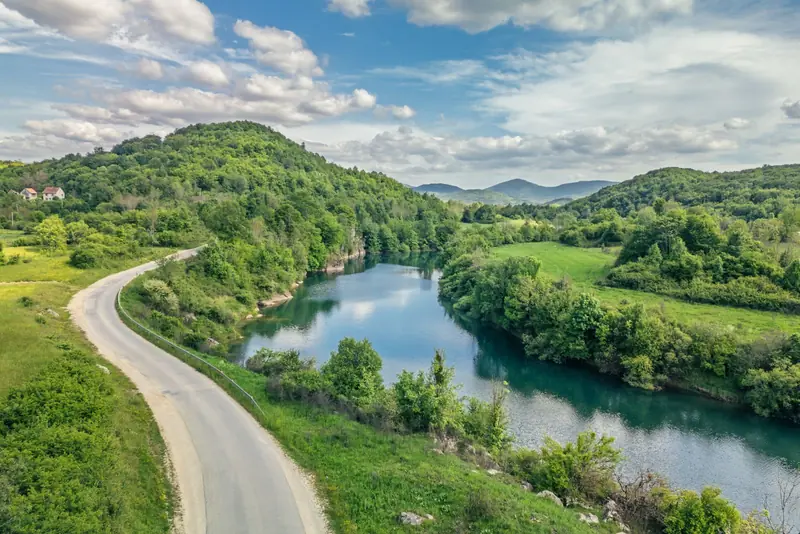 Prazna cesta prati zavoj zelene rijeke, snimljeno dronom