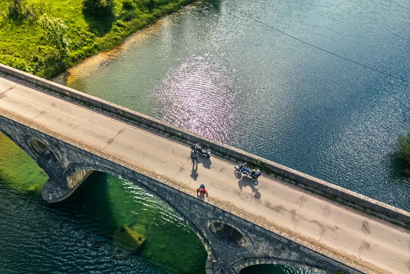 Motori prelaze stari kameni most iznad zelene rijeke