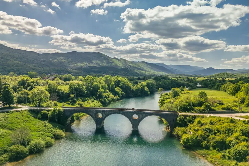 Stari kameni most preko rijeke, brda i oblaci u pozadini