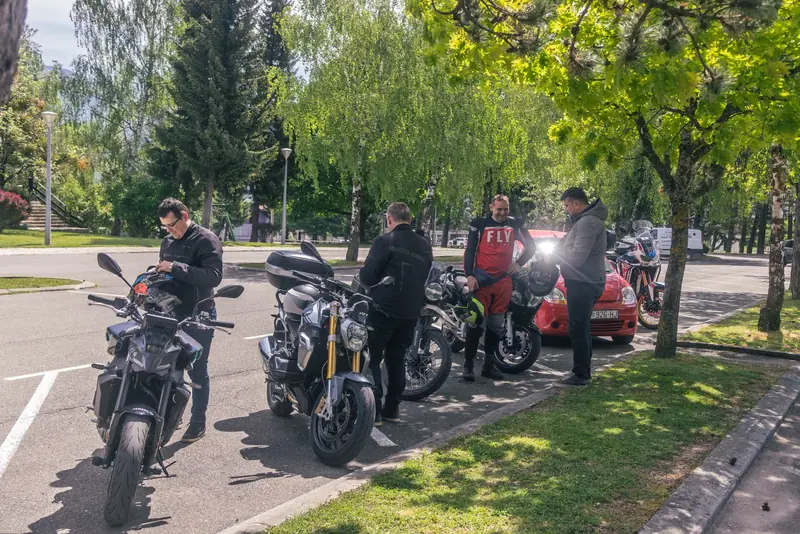 Motoristi stoje uz motore u hladu drveća na parkingu